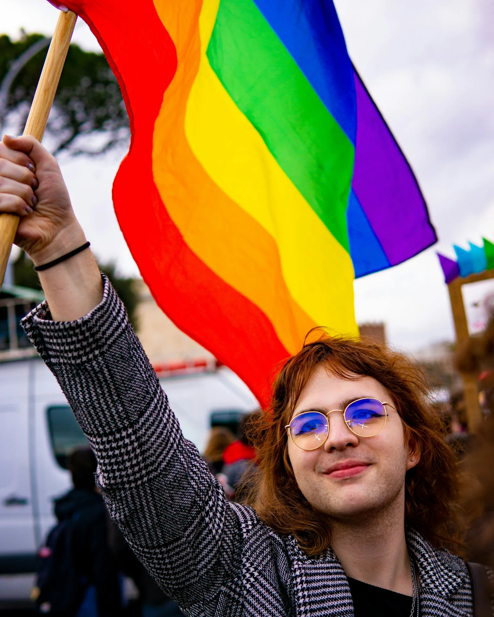 A young community member smiling with a rainbow flag