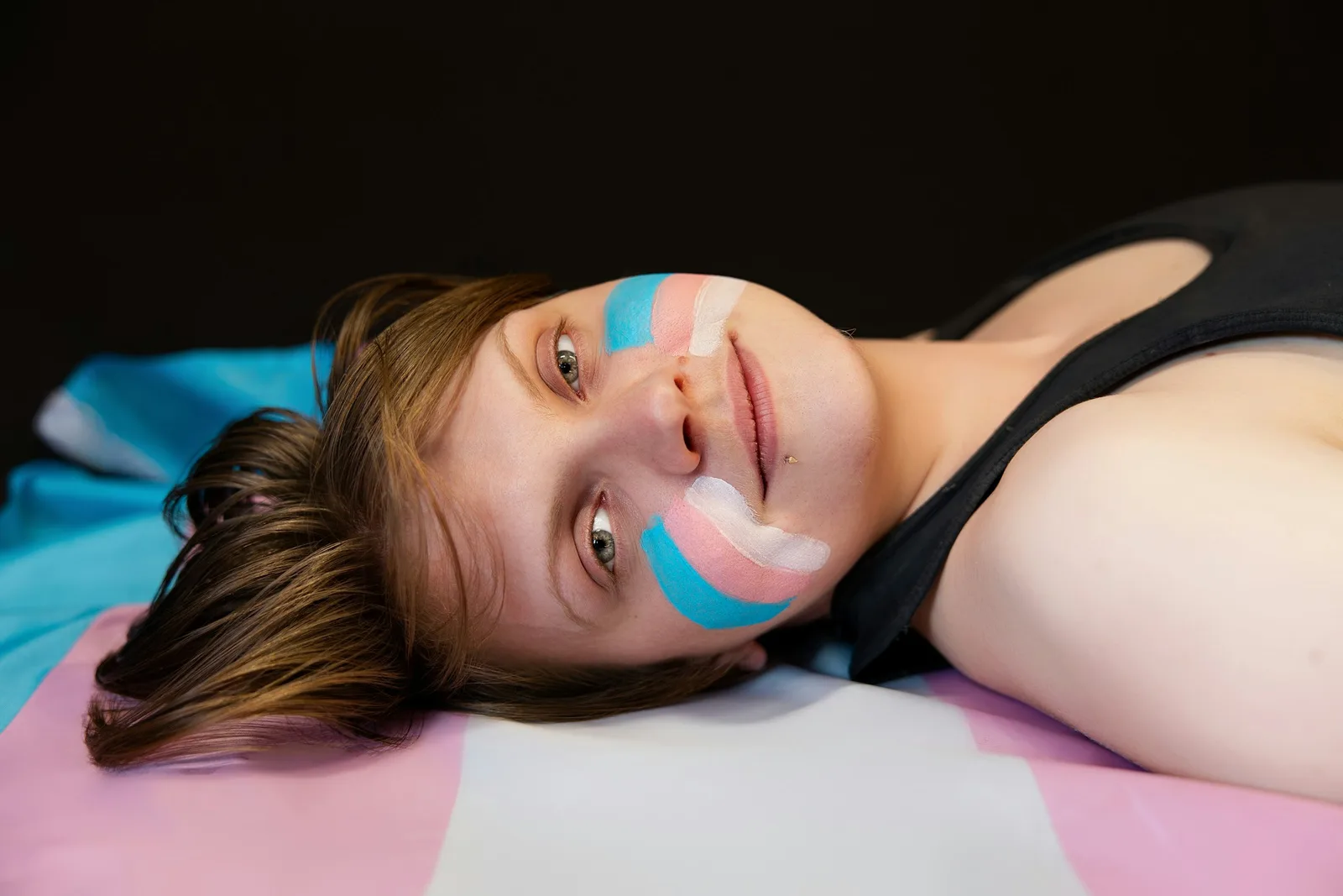 A trans community member resting on a trans-flag blanket, soft expression