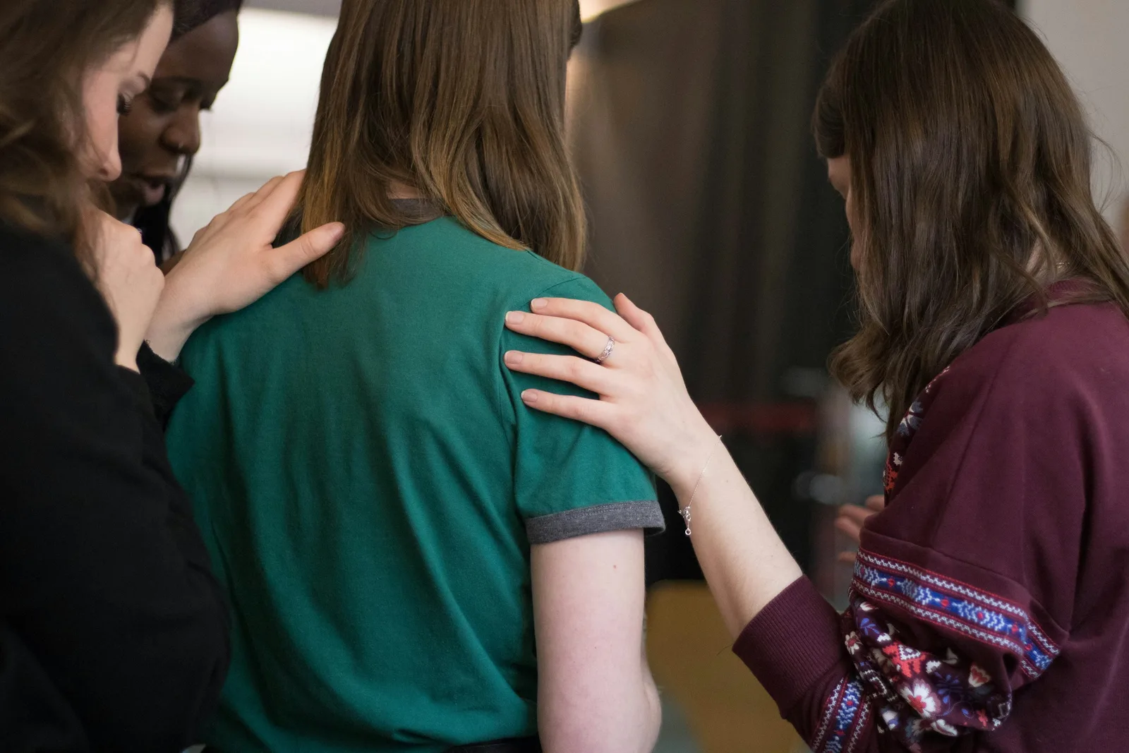 Three friends resting hands on one another in a quiet moment of support