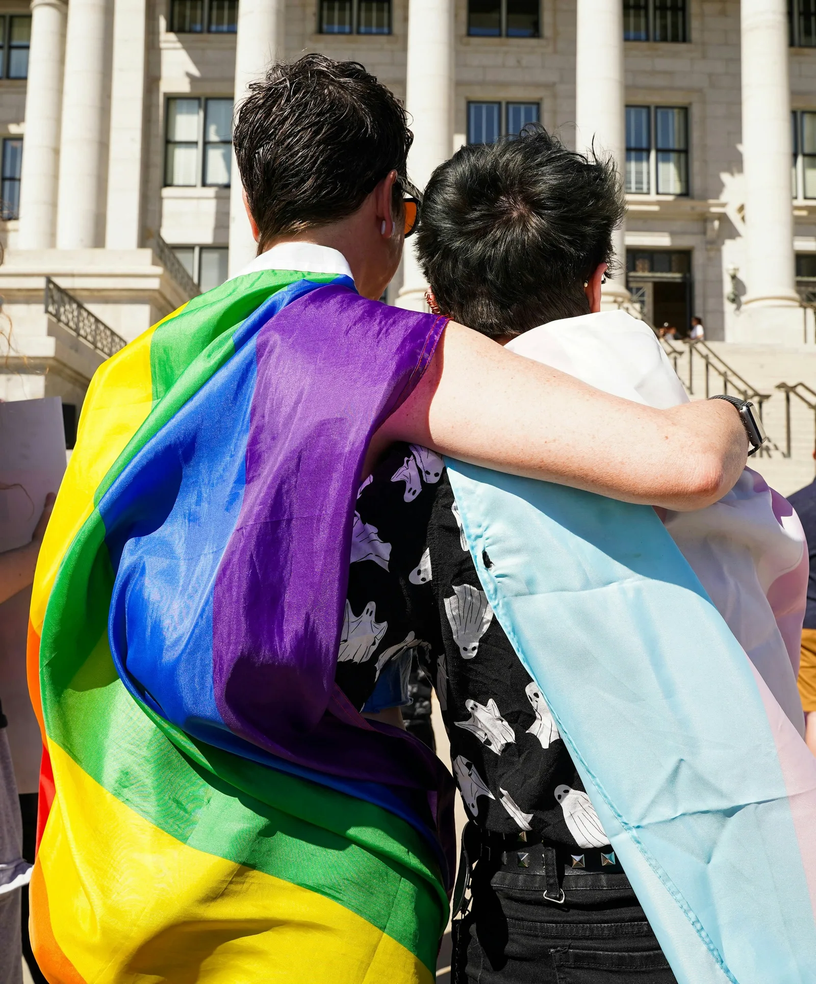 Two people embracing, wrapped in pride and trans flags